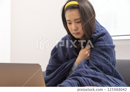 girl is sitting at sofa and working remotely on laptop. Female is blowing out snot, having fever and headache. Young woman is treated at home, took sick leave. Winter cold and flu concept girl is sitting at sofa and working remotely on laptop. Female is blowing out snot, having fever and headache. Young woman is treated at home, took sick leave. Winter cold and flu concept 125988042