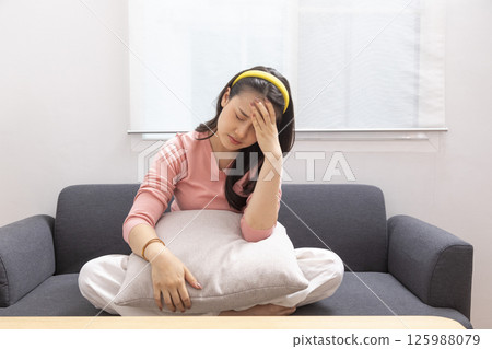 Asian woman are holding their hands to the head in pain on the sofa at home, Young women have severe headaches from migraines, Health and illness concept Asian woman are holding their hands to the head in pain on the sofa at home, Young women have severe headaches from migraines, Health and illness concept 125988079