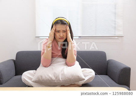 Asian woman are holding their hands to the head in pain on the sofa at home, Young women have severe headaches from migraines, Health and illness concept Asian woman are holding their hands to the head in pain on the sofa at home, Young women have severe headaches from migraines, Health and illness concept 125988080