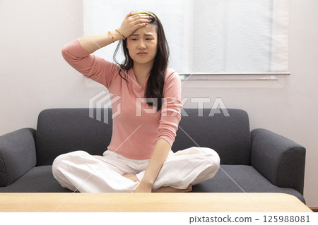 Asian woman are holding their hands to the head in pain on the sofa at home, Young women have severe headaches from migraines, Health and illness concept Asian woman are holding their hands to the head in pain on the sofa at home, Young women have severe headaches from migraines, Health and illness concept 125988081