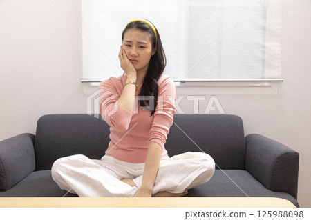 Asian young woman sitting on the sofa at home touching mouth with hand with painful expression because of toothache or dental illness on teeth. dentist Asian young woman sitting on the sofa at home touching mouth with hand with painful expression because of toothache or dental illness on teeth. dentist 125988098