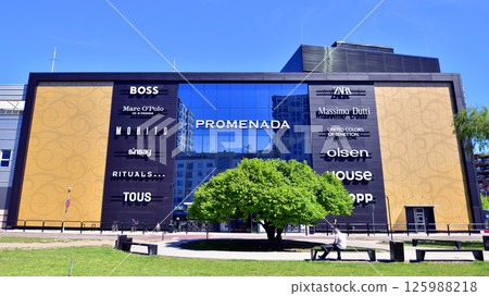 Warsaw, Poland. 1 May 2025. The front wall and the entrance door to the modern shopping center known as the Promenada in sunny day. 125988218