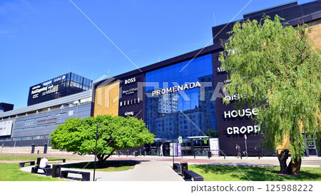 Warsaw, Poland. 1 May 2025. The front wall and the entrance door to the modern shopping center known as the Promenada in sunny day. Warsaw, Poland. 1 May 2025. The front wall and the entrance door to the modern shopping center known as the Promenada in sunny day. 125988222
