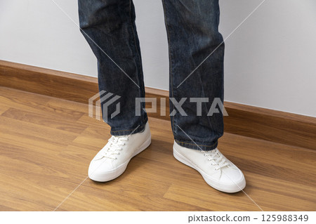 Feet wearing white chunky sole sneakers and blue jeans on the white wood floor 125988349