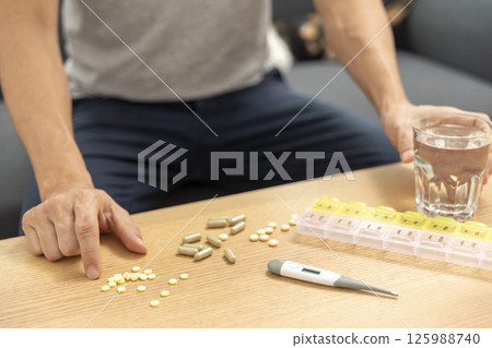 Young Asian man feeling sick and taking pills while sitting on the bed at home with medicines tablets and drinking water on table. Healthcare and Medicine concept Young Asian man feeling sick and taking pills while sitting on the bed at home with medicines tablets and drinking water on table. Healthcare and Medicine concept 125988740