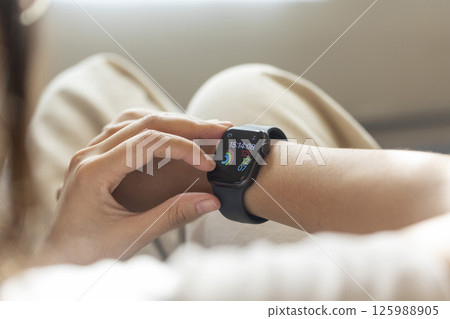 young woman using touchscreen smart watch sitting on sofa at Home. mixed race asian chinese model. young woman using touchscreen smart watch sitting on sofa at Home. mixed race asian chinese model. 125988905