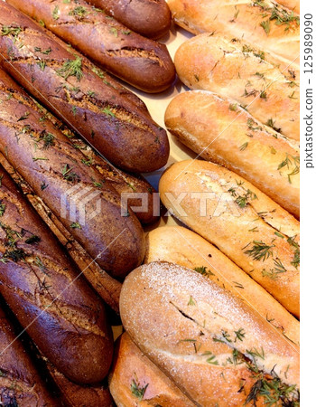 freshly baked bread loaves with herbs displayed on wooden surface in bakery setting. freshly baked bread loaves with herbs displayed on wooden surface in bakery setting. 125989090