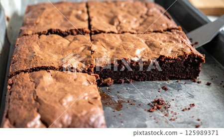 Freshly baked brownie sheet with visible knife cuts and piece being lifted, showcasing homemade treat 125989371