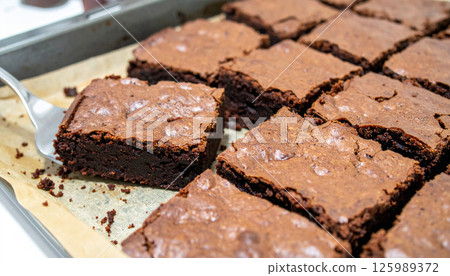 Freshly baked brownies with visible knife cuts, one piece being lifted from tray, showcasing homemade treat 125989372