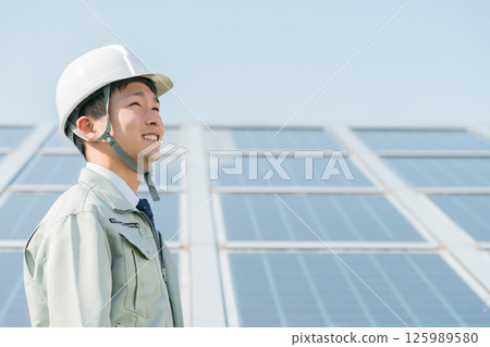 An engineer in work clothes from an electric power company or electrical contractor standing in front of a solar power generation/solar panel (clean energy) 125989580