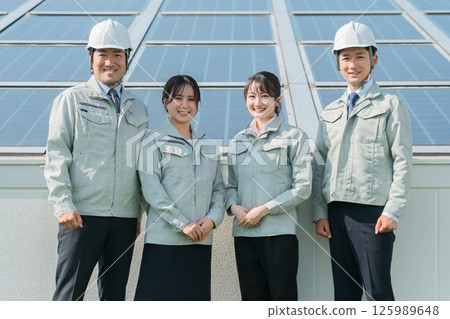 An engineer in work clothes from an electric power company or electrical contractor standing in front of a solar power generation/solar panel (clean energy) An engineer in work clothes from an electric power company or electrical contractor standing in front of a solar power generation/solar panel (clean energy) 125989648