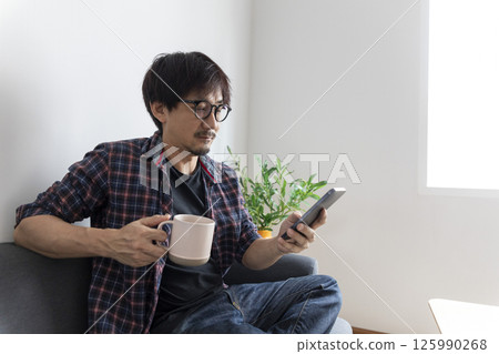 Happy asian young adult man sitting on sofa at living room reading fiction book. Domestic life relax at home. 125990268