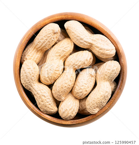 In-shell roasted peanuts in a wooden bowl. Whole, crunchy nut, fruits of Arachis hypogaea, encased in its natural shell. Light golden snack food with natural, nutty aroma, and firm, crunchy texture. 125990457