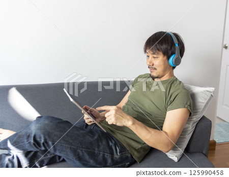 Man on sofa with headphones and digital tablet Man on sofa with headphones and digital tablet 125990458
