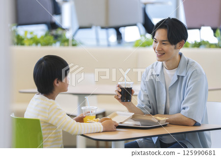 一對父子在美食廣場吃飯：一位 30 多歲的父親和一位小學男孩 125990681