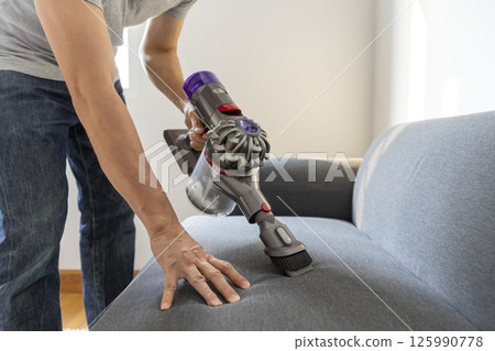 Adult Man in jeans and T-shirt vacuuming a sofa Adult Man in jeans and T-shirt vacuuming a sofa 125990778