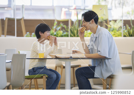 A parent and child eating hamburgers facing each other: a 9-year-old boy and his father in his 30s 125990852