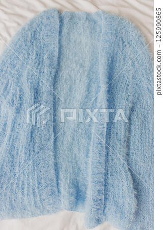 Blue knitted cardigan on white background. Soft blue knitted sweater in details. Knitting pattern background. Summer knitted fashion. Cozy hobby. Craft product concept.  125990865