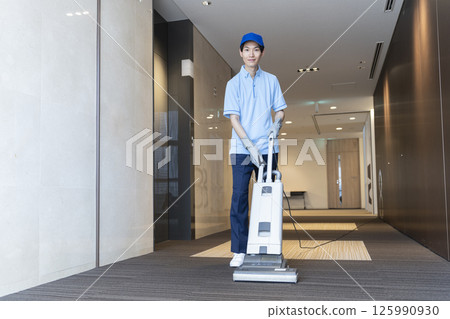 年輕男清潔人員正在打掃大樓,看著相機 年輕男清潔人員正在打掃大樓,看著相機 125990930