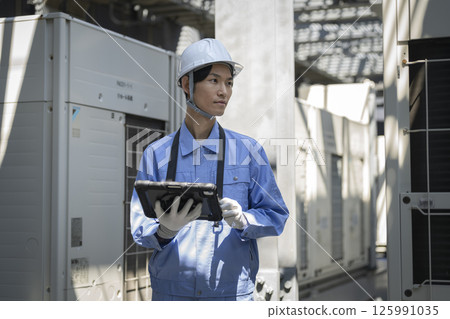 A man in work clothes inspects the outdoor air conditioning unit installed on the roof of a building. Building maintenance image. 125991035