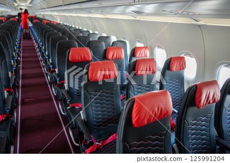 Empty interior of cabin of airplane with rows of black and red seats in daytime before the flight Empty interior of cabin of airplane with rows of black and red seats in daytime before the flight 125991204