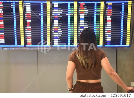 Asian woman carrying travel bag and look at airline schedule board in airport 125991617