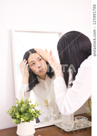 一位中年婦女在鏡子裡擔心自己的髮際線 一位中年婦女在鏡子裡擔心自己的髮際線 125991788