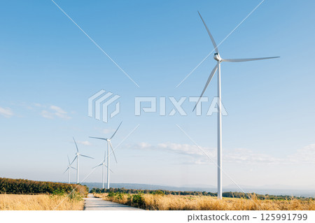 Amidst a winter meadow windmill farm turbines harness the wind's force for sustainable energy. Modern wind technology supporting a cleaner environment under a blue sky. 125991799