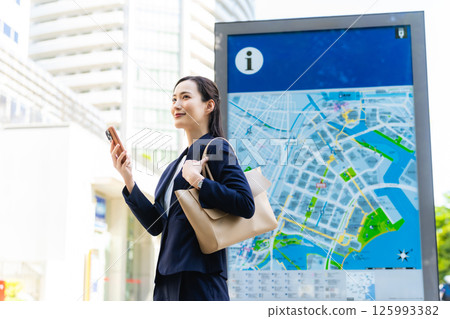 一位女商務人士透過查看地圖和智慧型手機來檢查位置 125993382