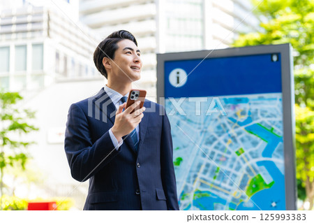 A male business person checking a location by looking at a map and smartphone 125993383
