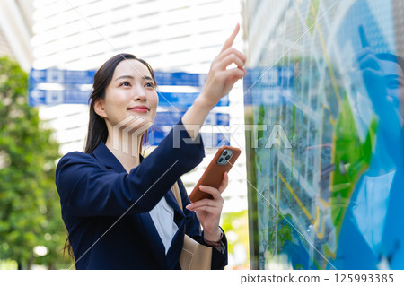 A female business person checking the location by looking at a map and smartphone A female business person checking the location by looking at a map and smartphone 125993385