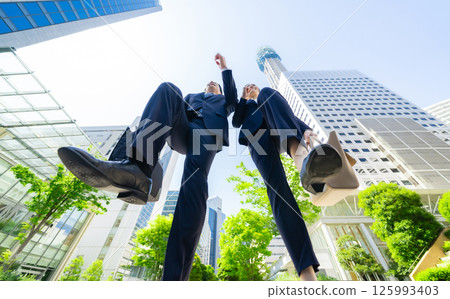 An up-close shot of a group of business people jumping in a city with fresh greenery 125993403