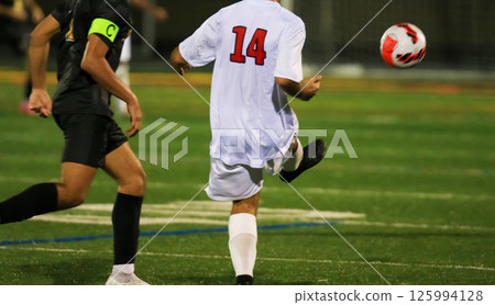 Player Kicks Soccer Ball During Match at a night game under the lights Player Kicks Soccer Ball During Match at a night game under the lights 125994128