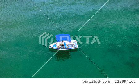 Small Boat With Blue Canopy Floating on Calm Green Waters Small Boat With Blue Canopy Floating on Calm Green Waters 125994163