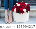 A luxurious bouquet of red and white roses is in a decorative gift box beside a stylishly woman legs in sparkly shoes. Valentines Day, flower store, shop, mock-up, delivery flowers, blog posts 125994217