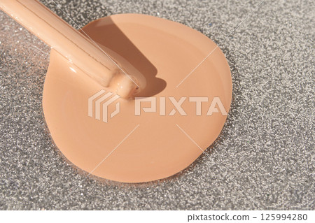 Liquid foundation poured on sparkling silver glitter background 125994280