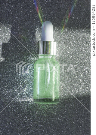 Glittering serum bottle with iridescent glow and light reflections on silver Glittering serum bottle with iridescent glow and light reflections on silver 125994282