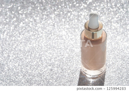 Shimmering bottle of skincare serum with dropper on sparkling glitter background 125994283