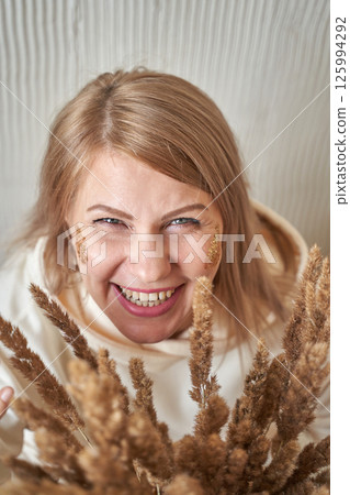 Smiling caucasian female adult holding dried wheat stalks indoors with autumnal Smiling caucasian female adult holding dried wheat stalks indoors with autumnal 125994292