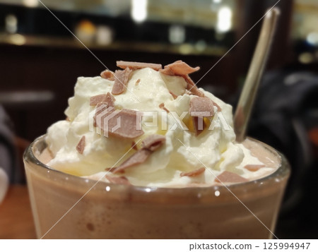 Hot chocolate with cream on top in a transparent glass close view background 125994947