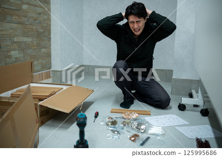 Japanese man holding his head while looking at assembling furniture 125995686