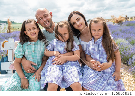 The light dresses of the mother and daughters contrast with the bright purple flowers. The light dresses of the mother and daughters contrast with the bright purple flowers. 125995931