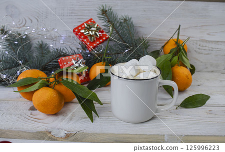 Cup of hot chocolate with marshmallows, tangerines and Christmas decorations on white wooden background. Cup of hot chocolate with marshmallows, tangerines and Christmas decorations on white wooden background. 125996223