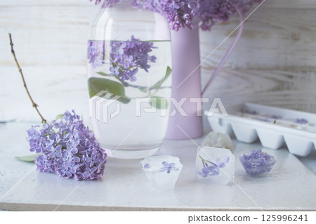 Lilac flowers, ice cubes and a glass of water on a light background and lilac flowers in a vase Lilac flowers, ice cubes and a glass of water on a light background and lilac flowers in a vase 125996241