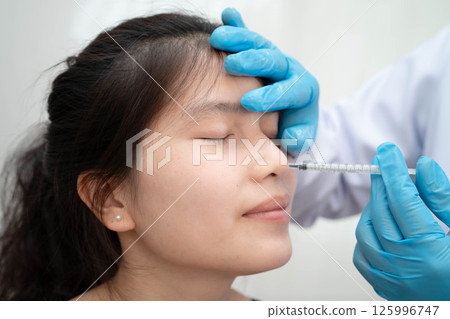 Asian woman receiving plastic surgery shape of nose performed on face. Asian woman receiving plastic surgery shape of nose performed on face. 125996747