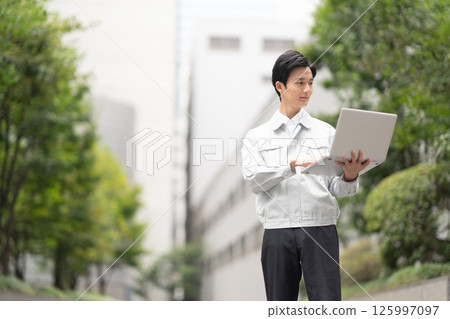 A man wearing work clothes and holding a computer 125997097