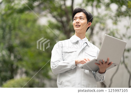 A man wearing work clothes and holding a computer 125997105