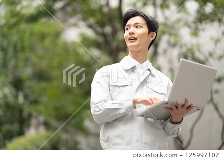 A man wearing work clothes and holding a computer 125997107