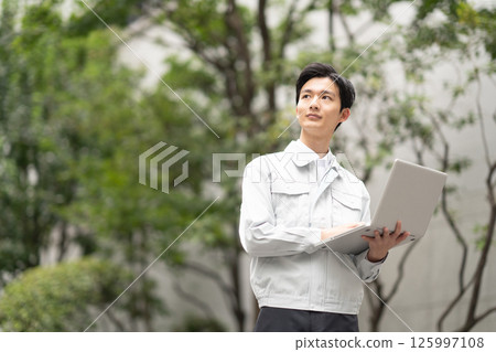 A man wearing work clothes and holding a computer 125997108