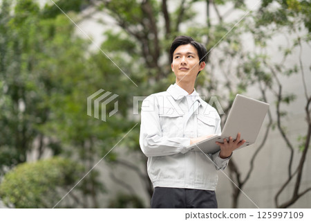 A man wearing work clothes and holding a computer 125997109